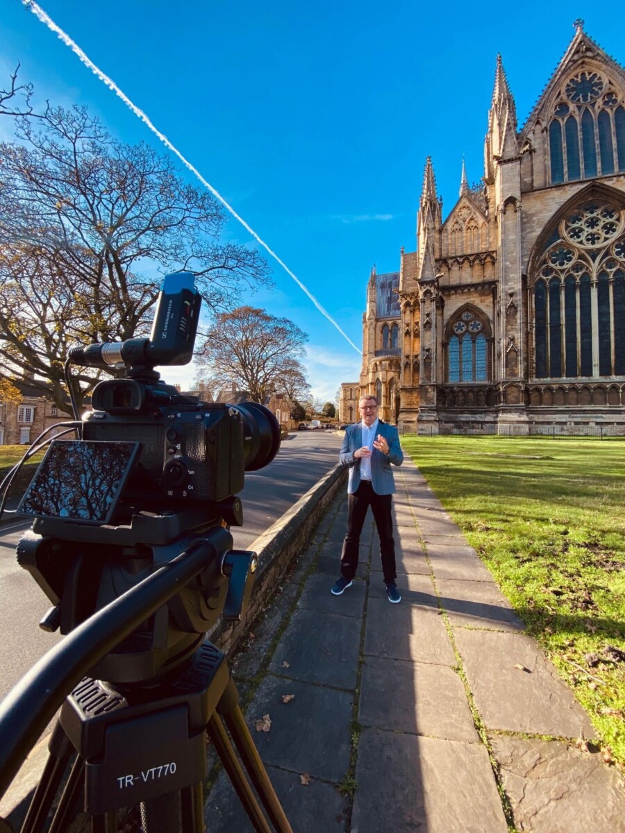 tall man stood outside of Lincoln cathedral in front of a camera