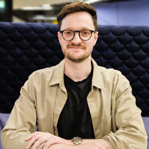 headshot image of Alex Spooner - a man in a camel shirt with glasses on